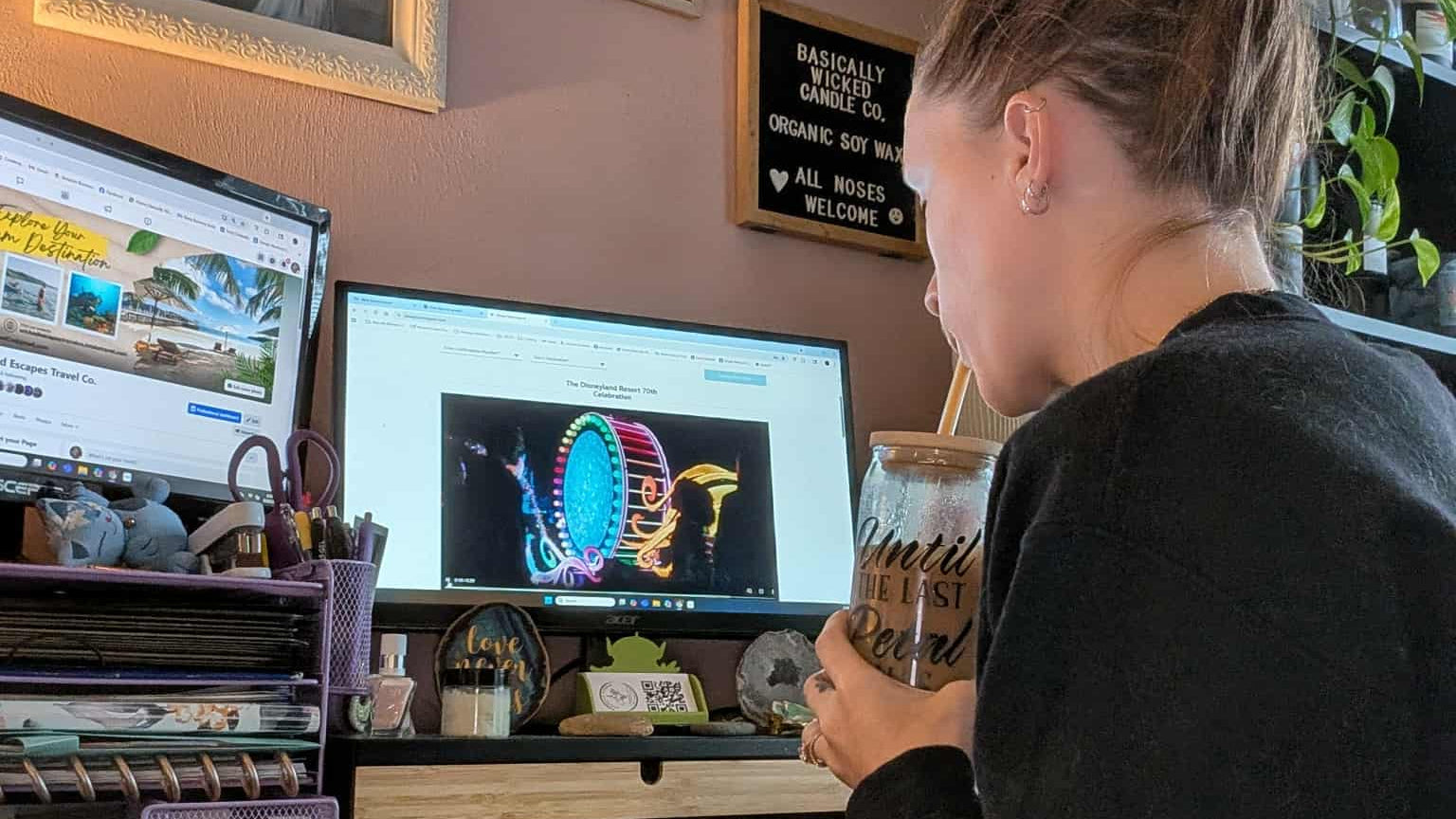 Person sitting at a desk with two computer monitors, surrounded by decor including framed pictures and plants.